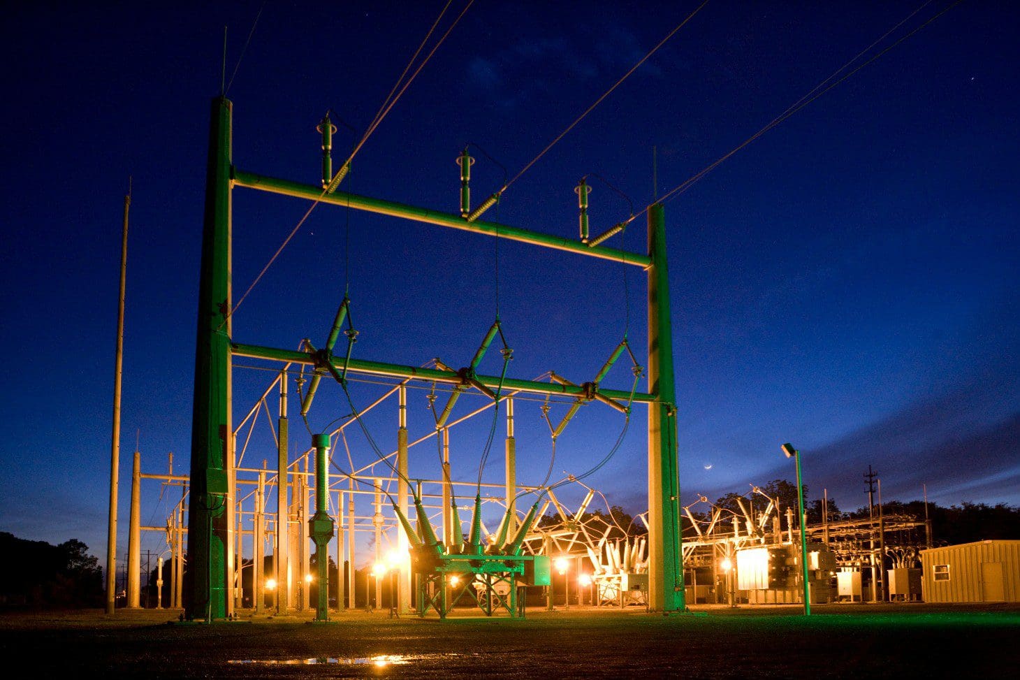 A large green power line tower at night.